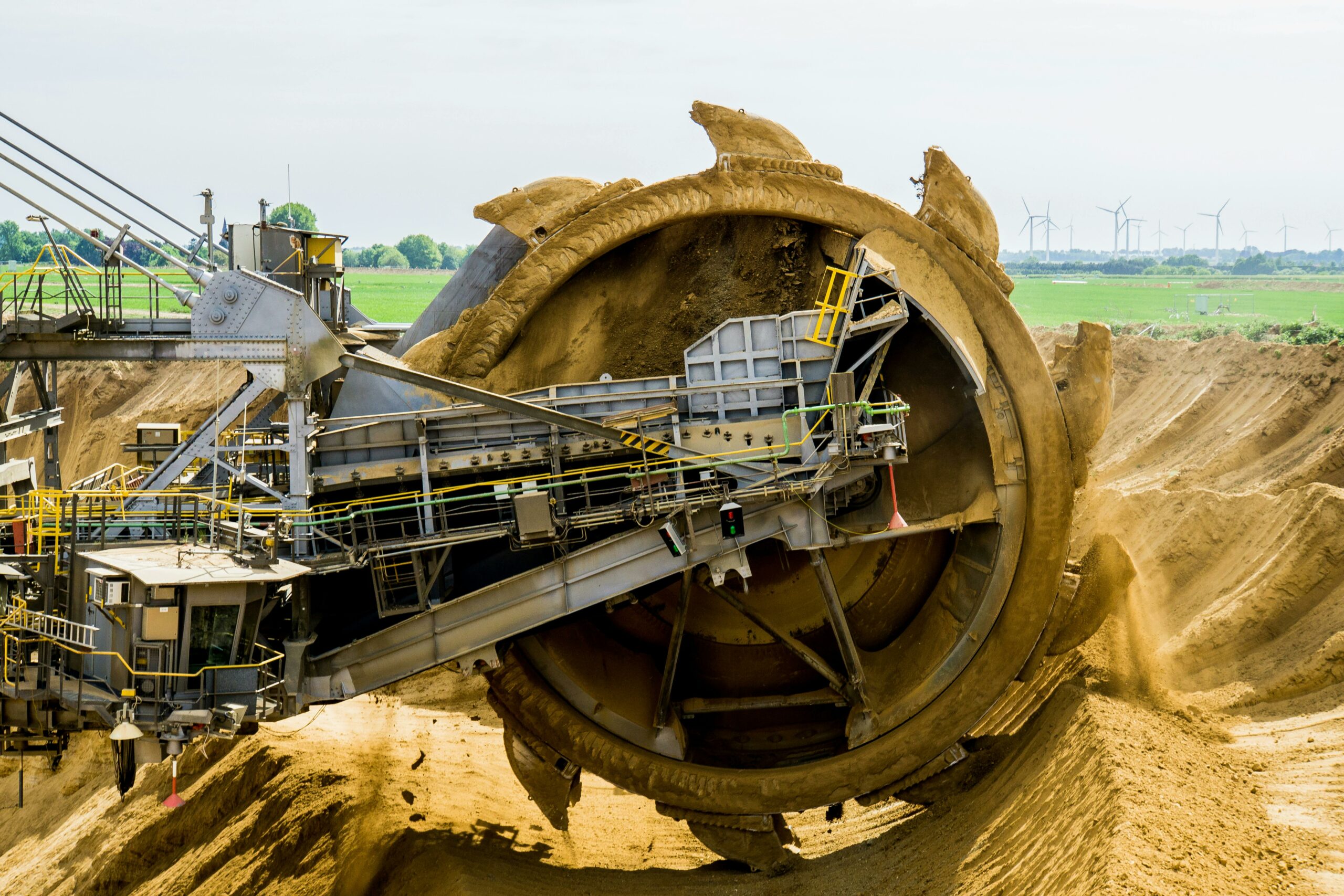 A large bucket wheel excavator working in an open pit mine against a green landscape.